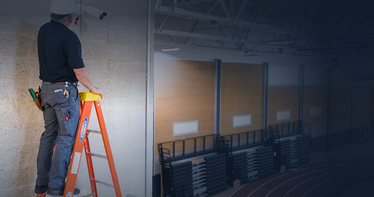 Construction worker installing alarm system into ceiling.