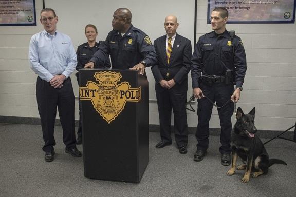 Sonitrol K-9 sits beside row of police officers at podium