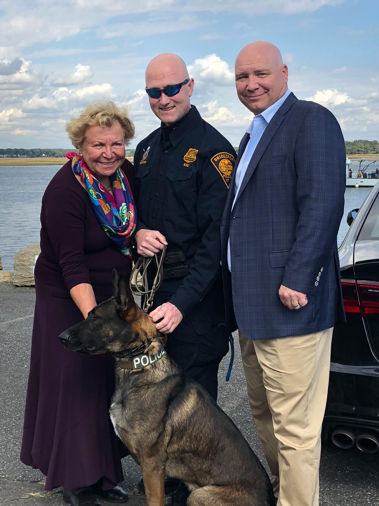 K-9 Dennis sits beside police officer and others