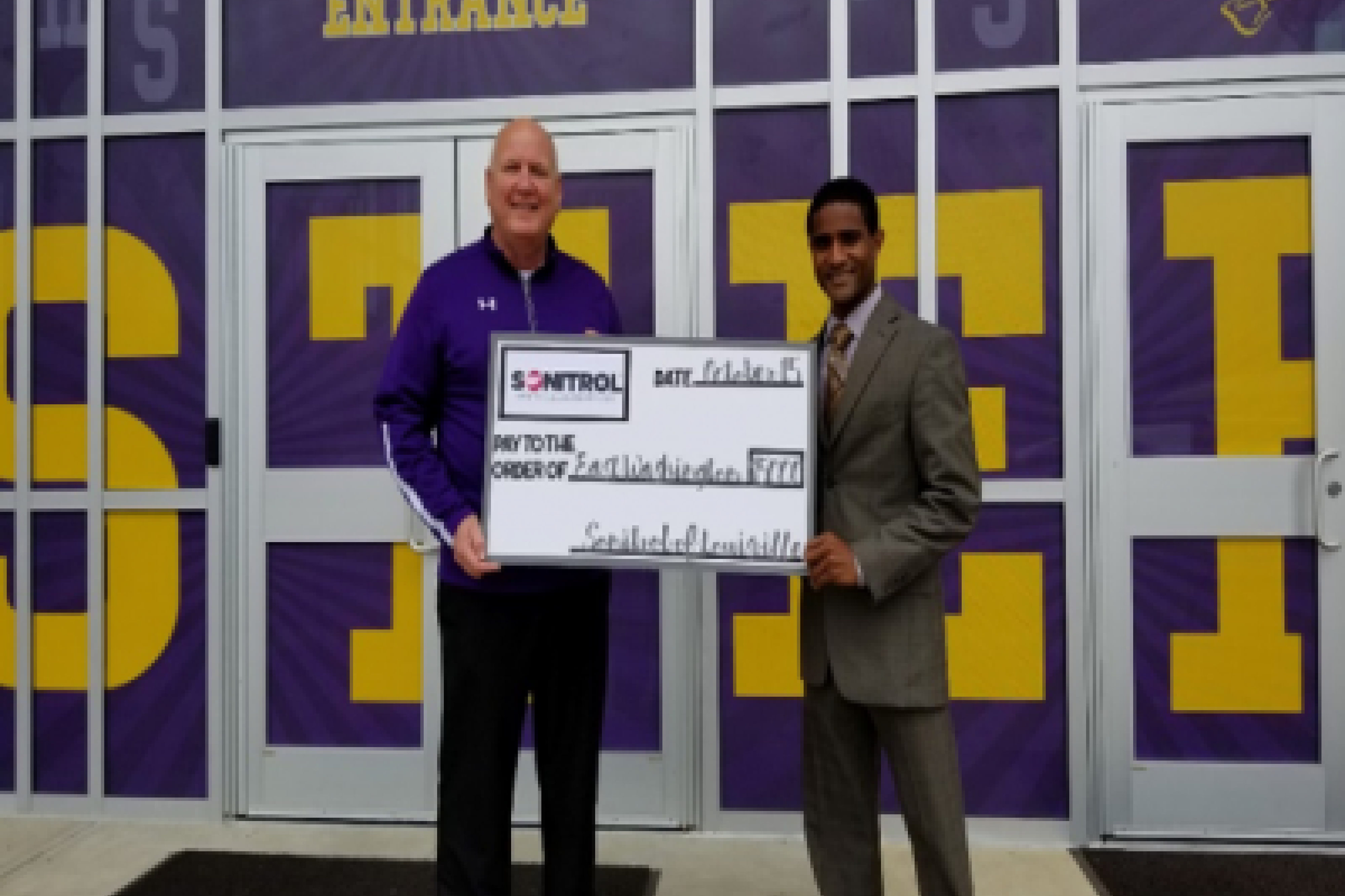 Sonitrol representative handing a giant check to a faculty member of a local S.T.E.M. Program.