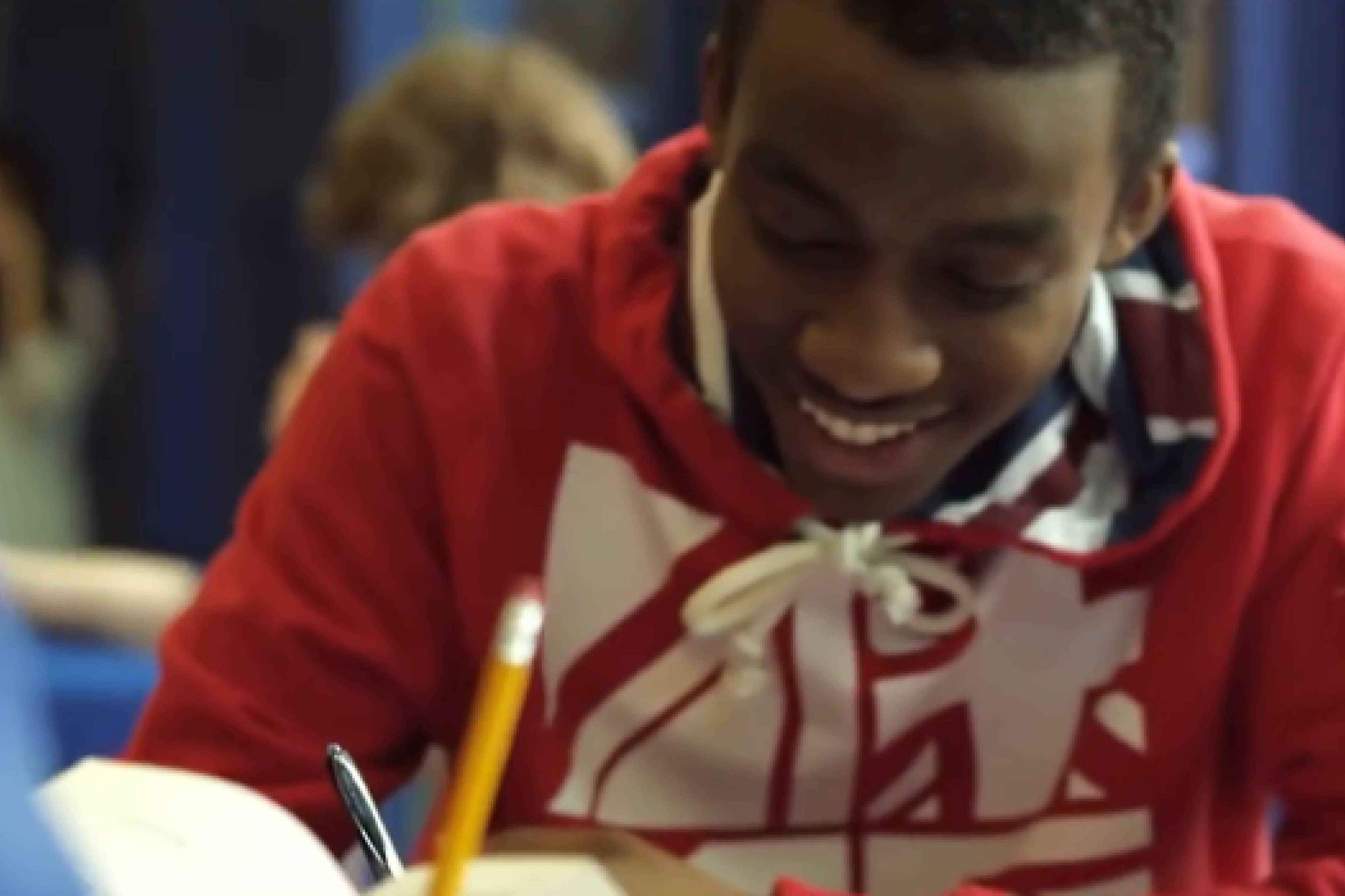 young man in red sweatshirt sitting at his desk at school writing with pencil