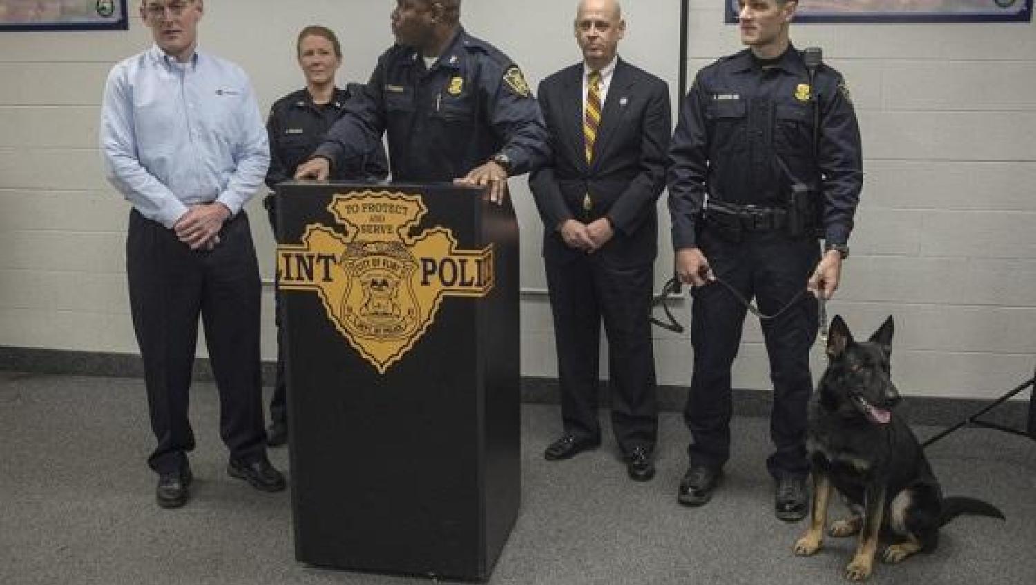 Sonitrol K-9 sits beside row of police officers at podium