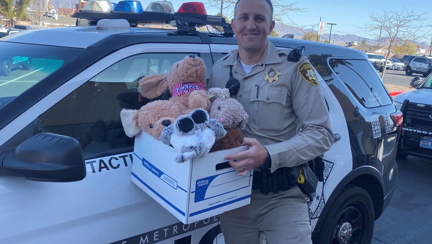 Officer in front of police car with office depot box of stuffed animals