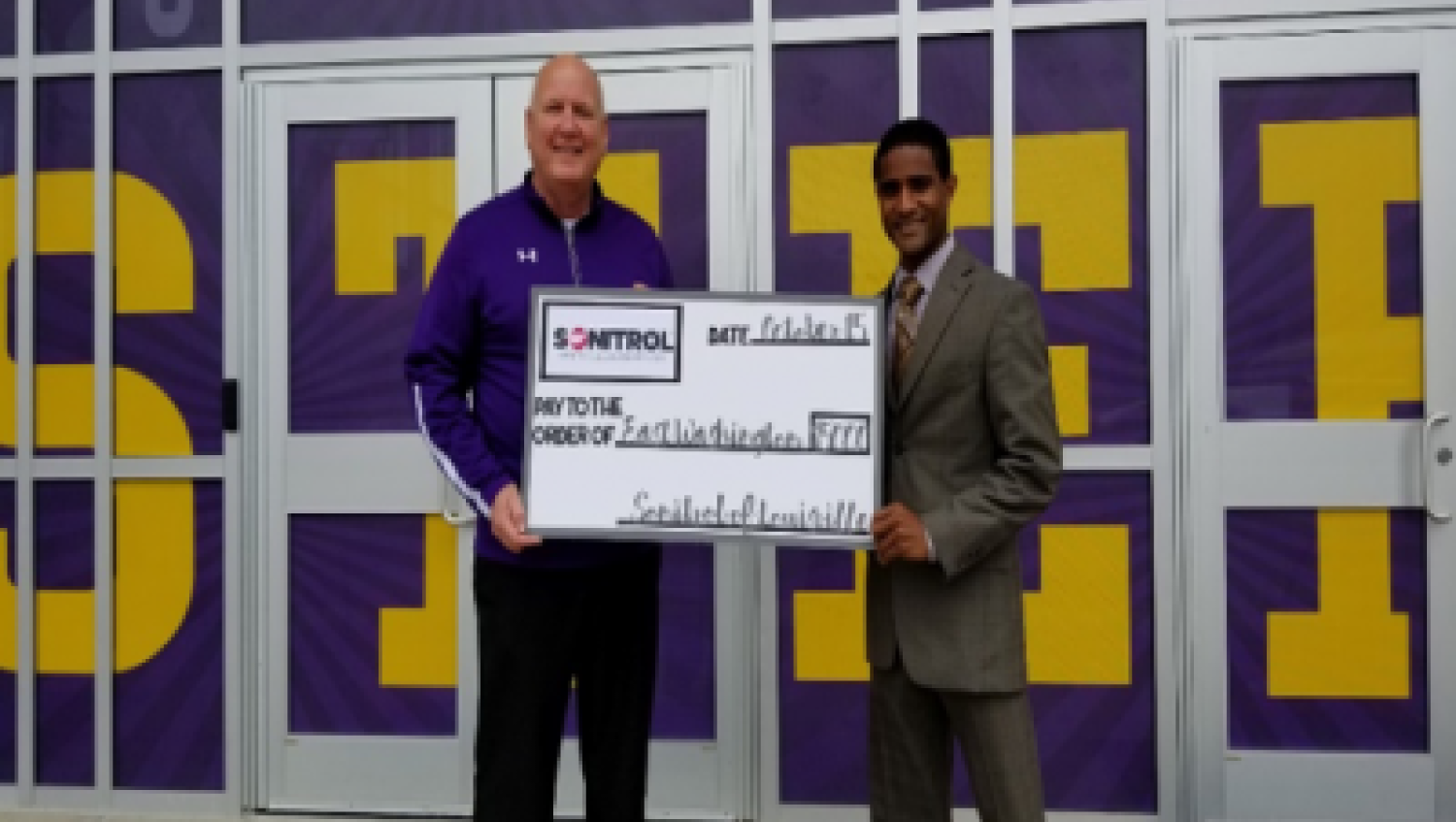 Sonitrol worker and school member holding giant donation check