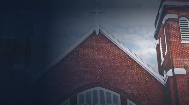 Front of a brick church with a white roof and cross on top.