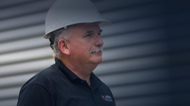 Sonitrol technician wearing hard hat near a white wall.