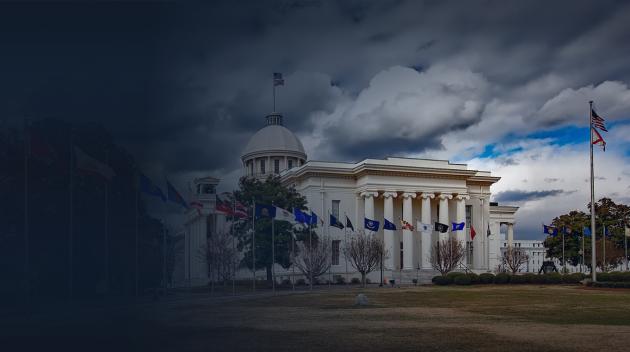 Side of a white government building with flags and a courtyard.