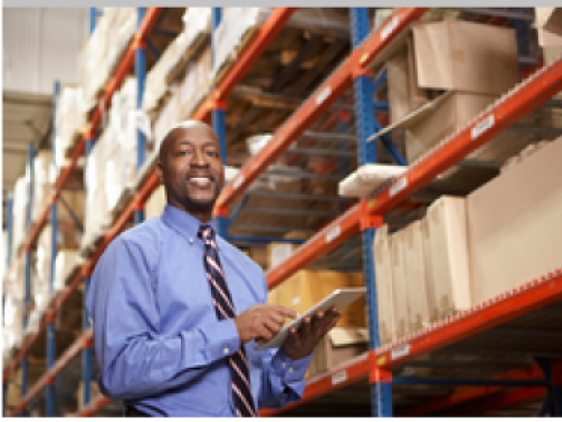 Smiling man in shirt and tie stands next to warehouse shelves.