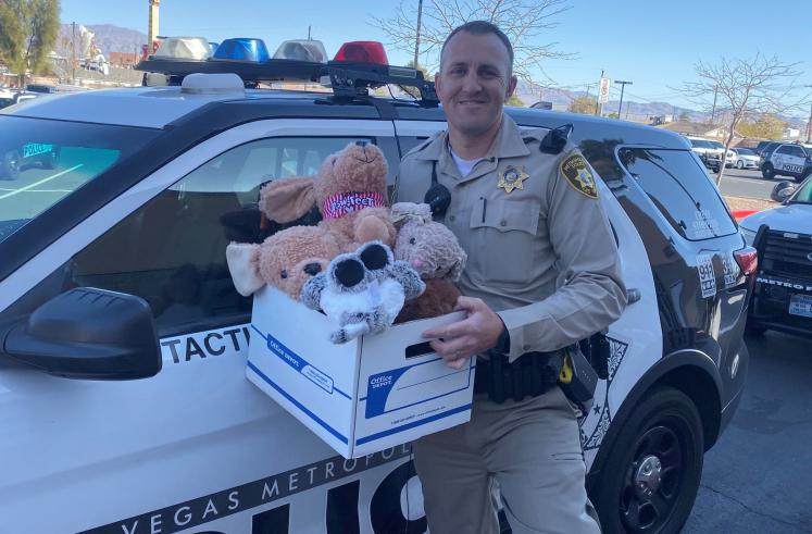 Officer in front of police car with office depot box of stuffed animals